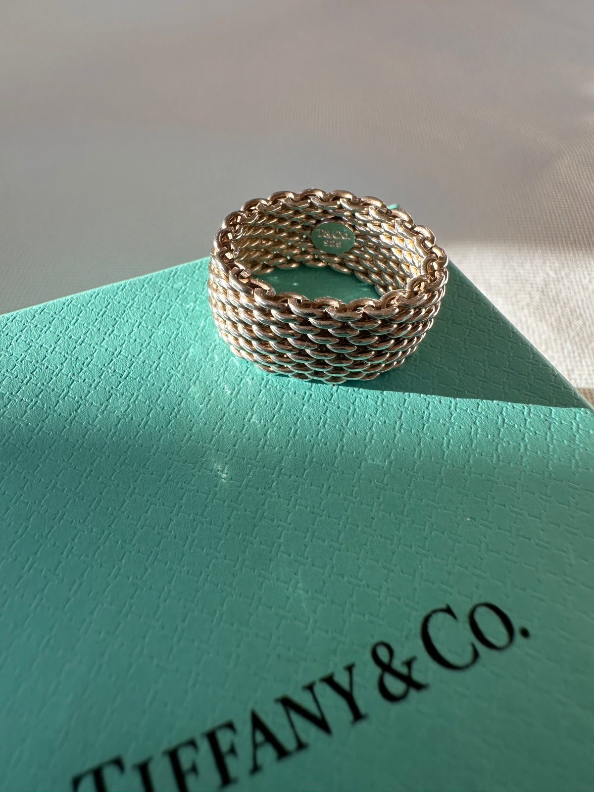 Angled view of the silver mesh ring on a Tiffany & Co. box, showing the woven band and interior marking.