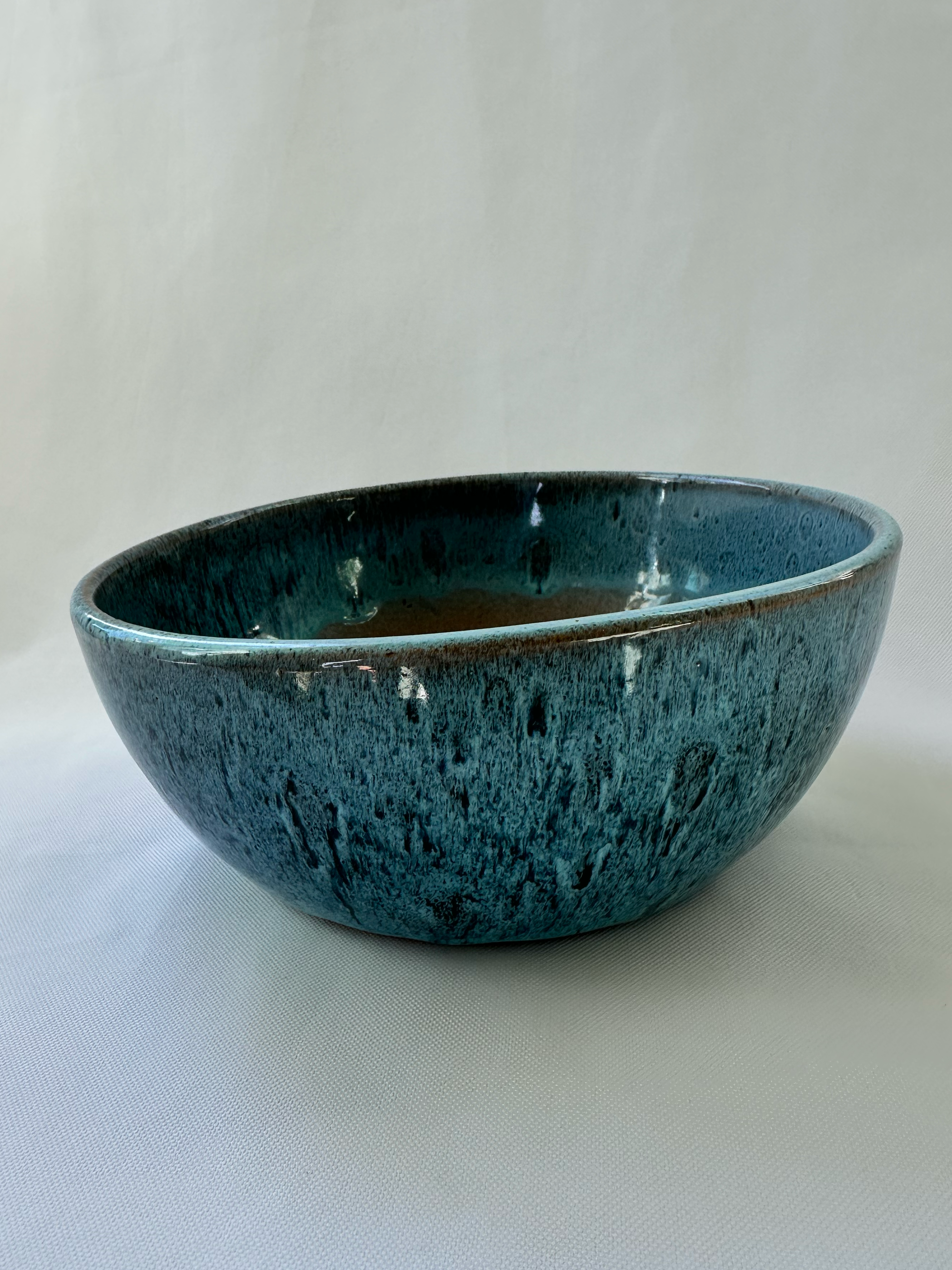 Three-quarter view of shallow blue glazed ceramic planter showing its rounded bowl shape and deep teal mottled finish.