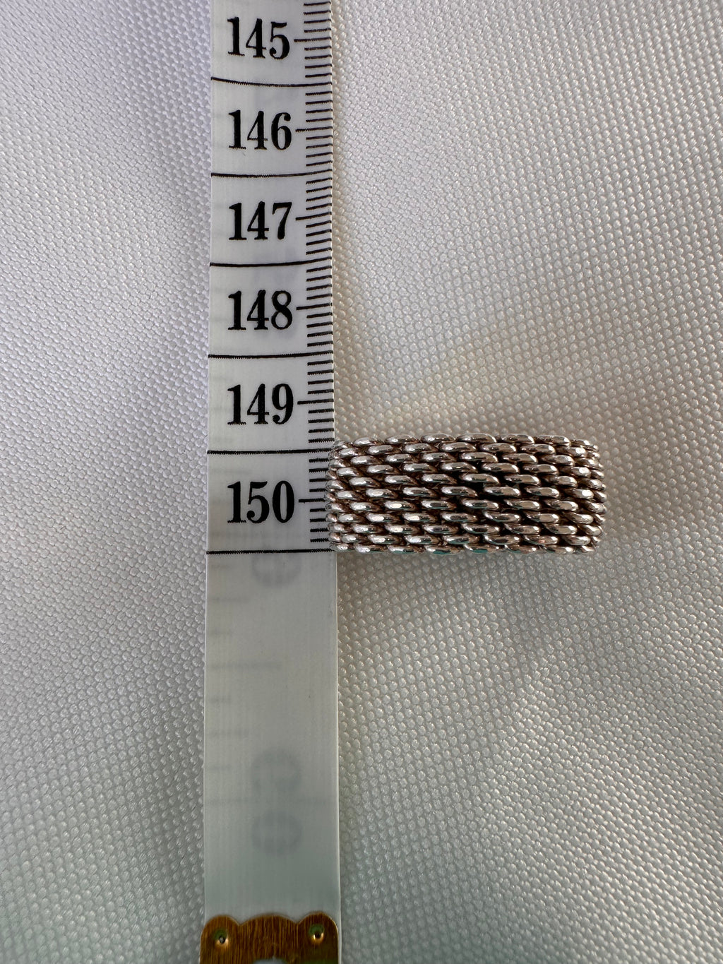 Side view of the silver mesh ring beside a measuring tape to show the width of the band.