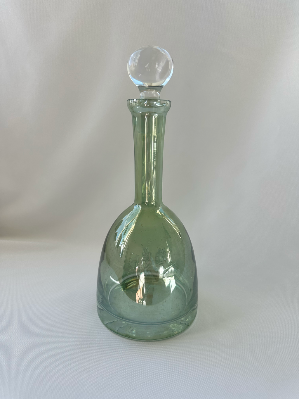 Alternate front view of green glass decanter showing rounded teardrop body and clear ball stopper.
