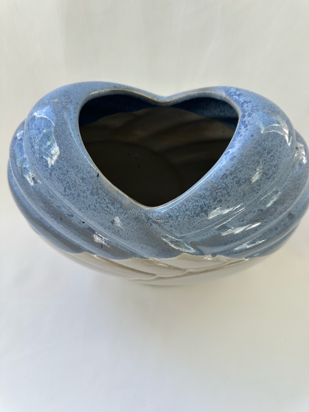 Angled view of blue glazed ceramic vase showing the heart-shaped opening and dimensional overlapping bands.
