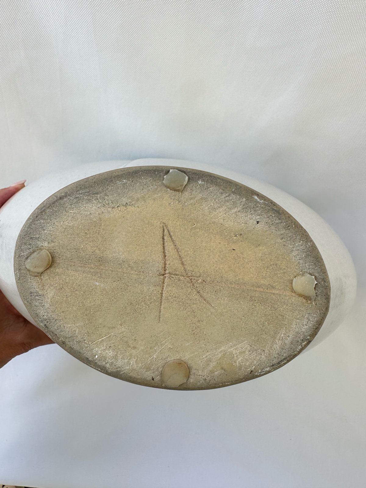 Bottom of ceramic vase showing the unglazed base and incised capital A maker mark.
