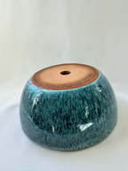 A handmade ceramic planter or bowl with a glossy teal-blue glaze and a natural brown clay base, shown on a white fabric background.
