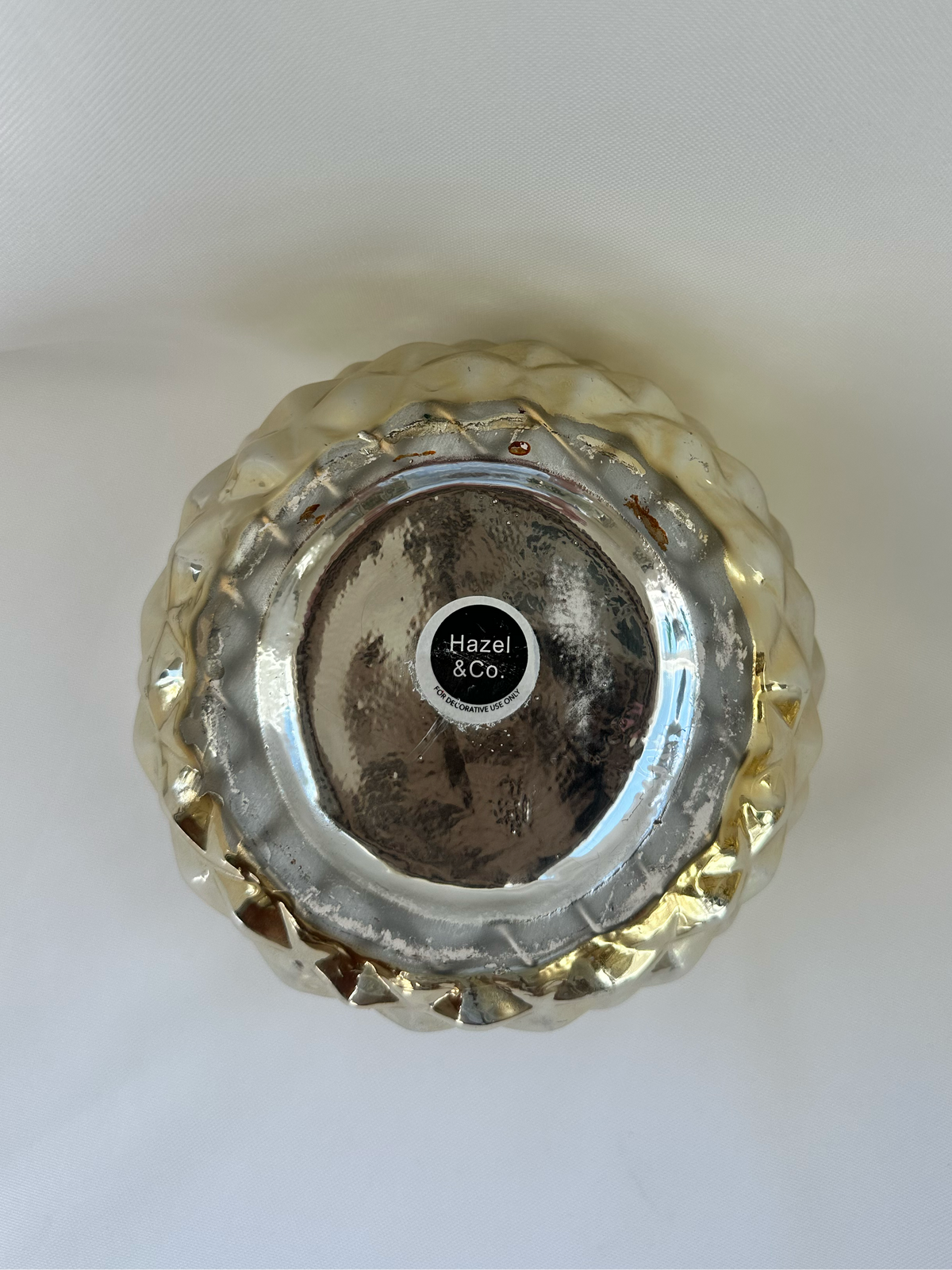 Bottom of Hazel & Co gold pineapple container showing maker label, decorative-use-only statement, and visible base wear.