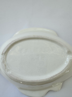 An off-white ceramic oval dish with scalloped sides, photographed from above on a white textured fabric background.