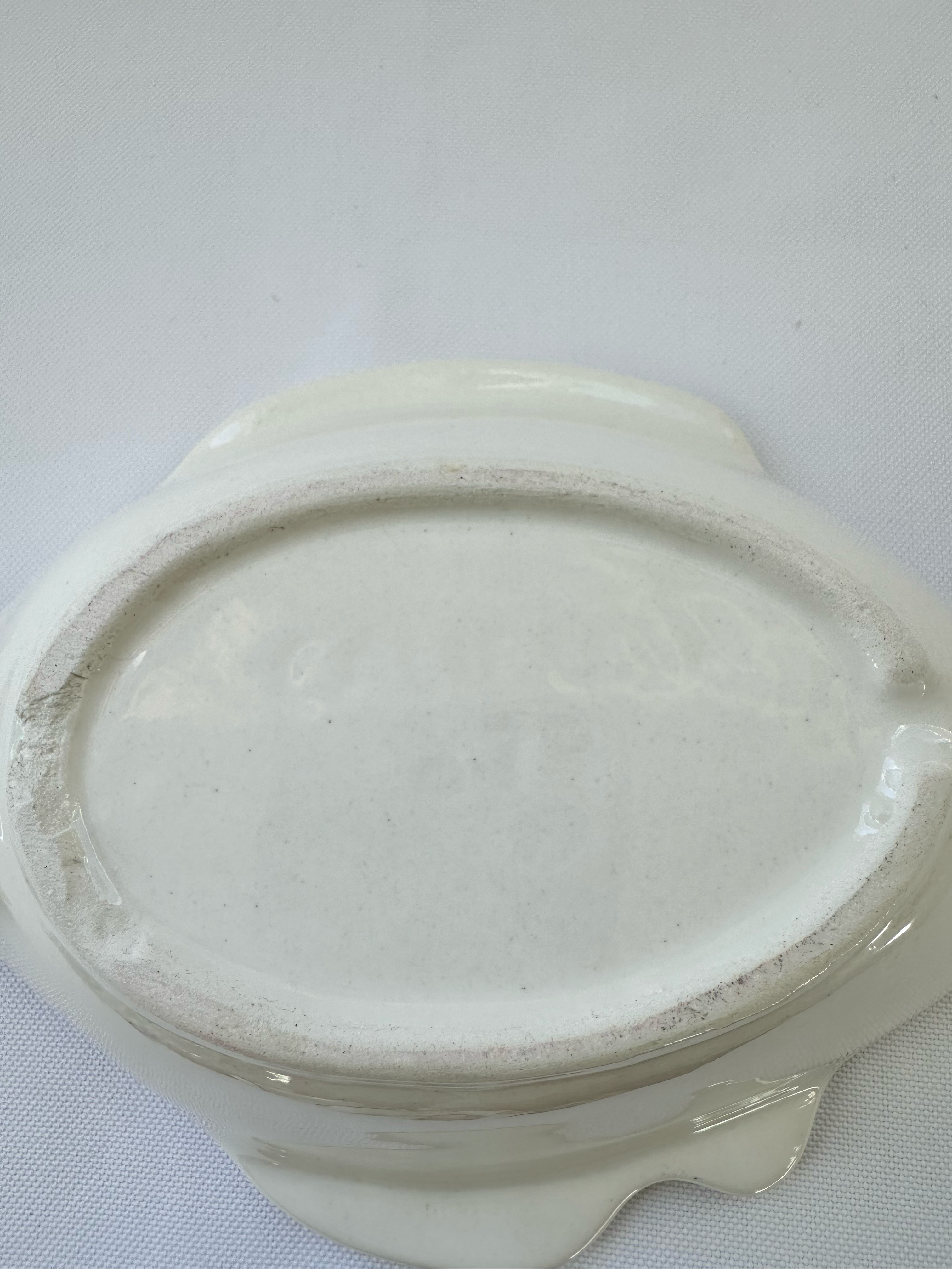 An off-white ceramic oval dish with scalloped sides, photographed from above on a white textured fabric background.