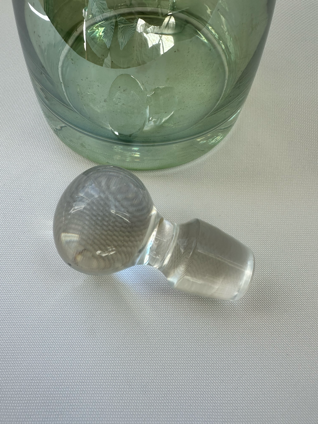 Clear glass globe stopper removed from green decanter, showing tapered stopper stem and rounded top.

