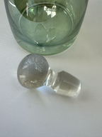 Clear glass globe stopper removed from green decanter, showing tapered stopper stem and rounded top.
