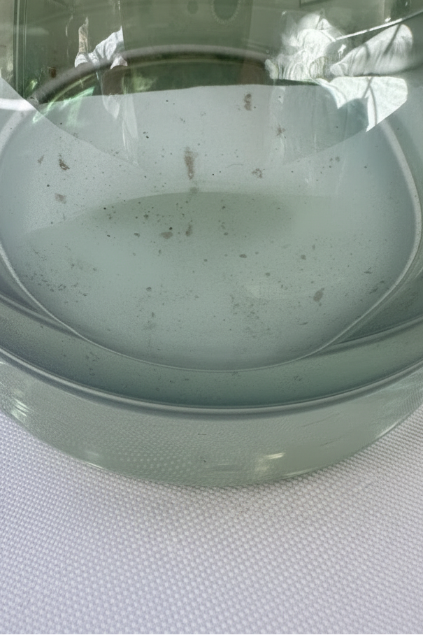 Close-up of lower green glass decanter body showing light gray spotting and interior discoloration near the base.

