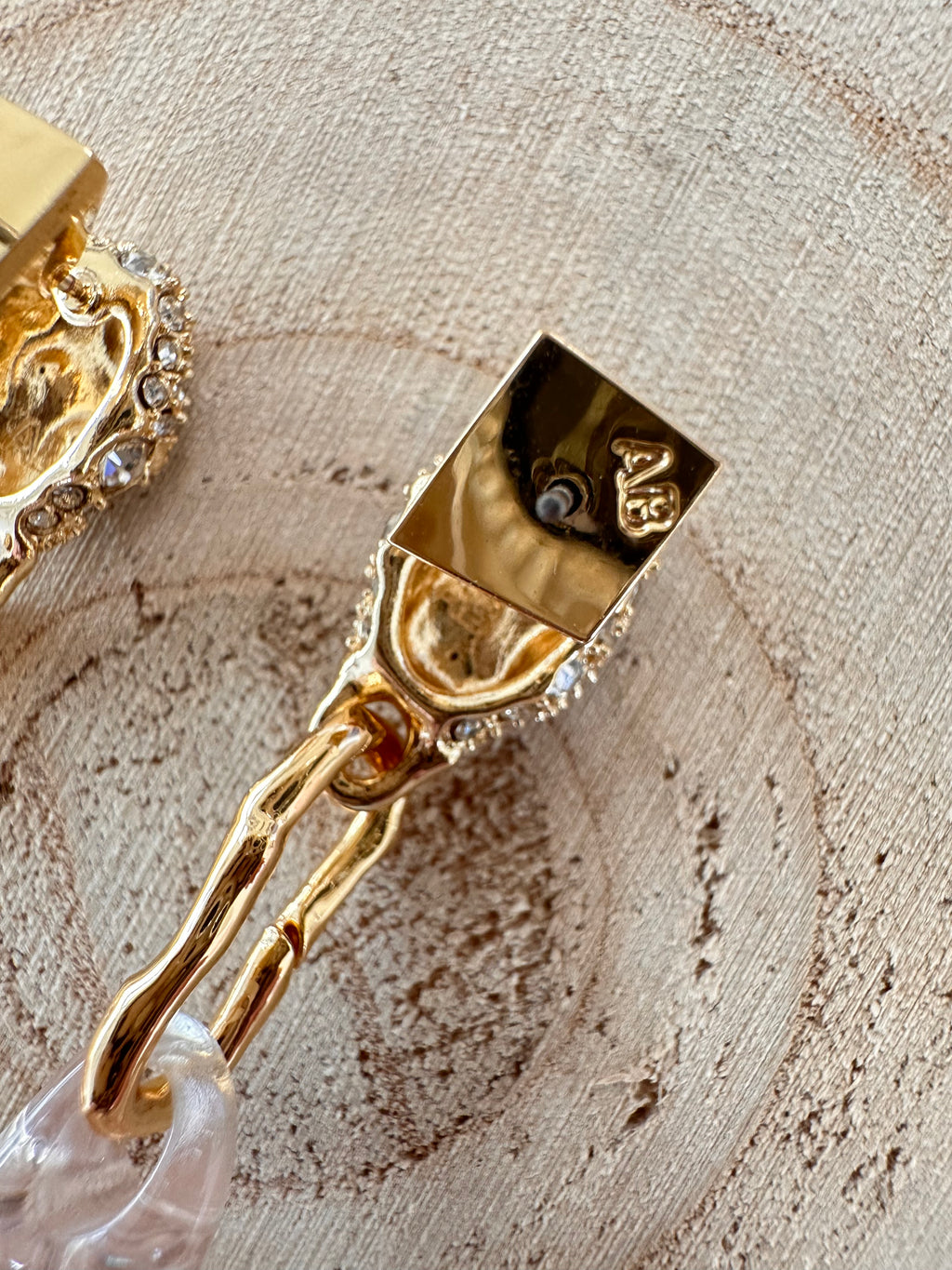 Close-up of the back of an Alexis Bittar drop earring showing the AB hallmark, post, and gold-tone link.
