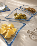 3 clear bowls with blue rims sit on a cocktail table holding olives, fresh lemon wedges and dried lime wheels. 