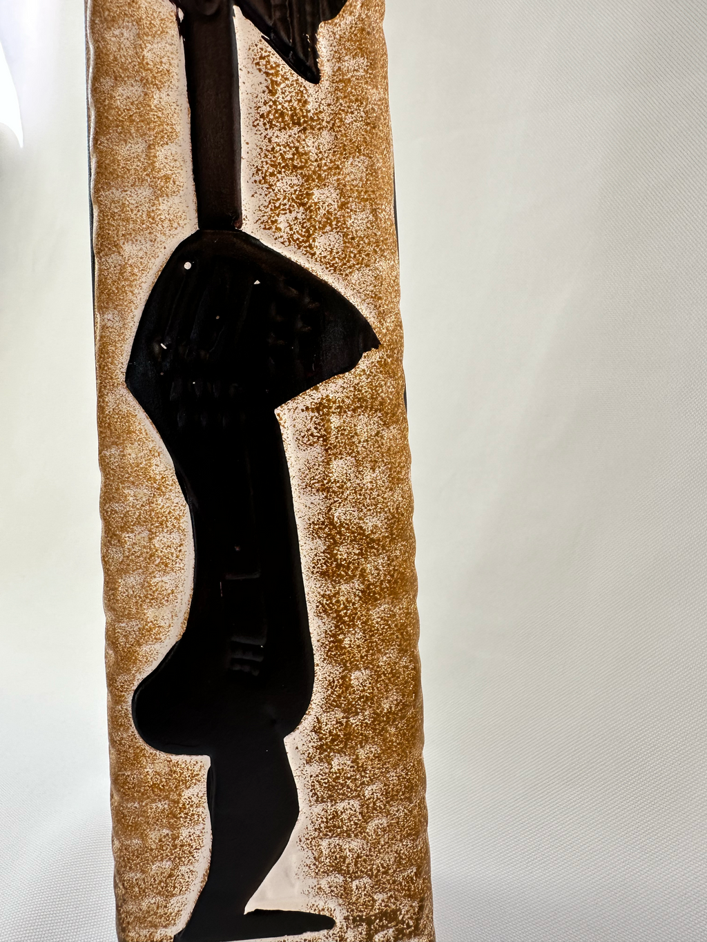 Close-up of raised black figural decoration on textured warm-toned ceramic vase showing small pock marks. 
