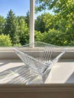 Tiffany & Co. Metropolis bowl sitting on a white windowsill, catching bright sunlight and casting rainbow reflections. A white window frame and a lush green outdoor background are visible behind it.
