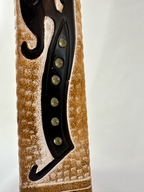 Close-up of raised black motif with muted green circular accents on textured ochre ceramic.
