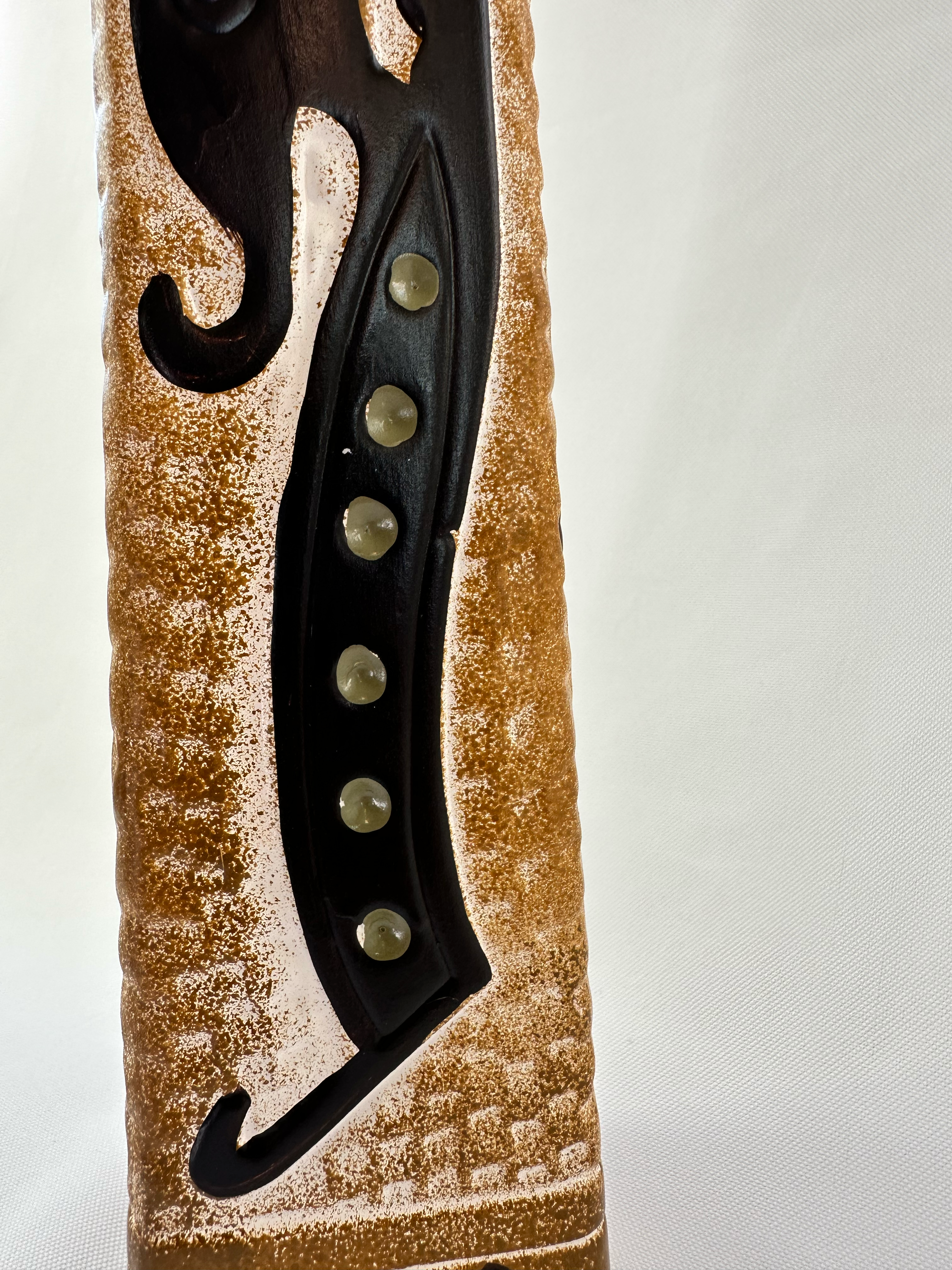 Close-up of raised black motif with muted green circular accents on textured ochre ceramic.
