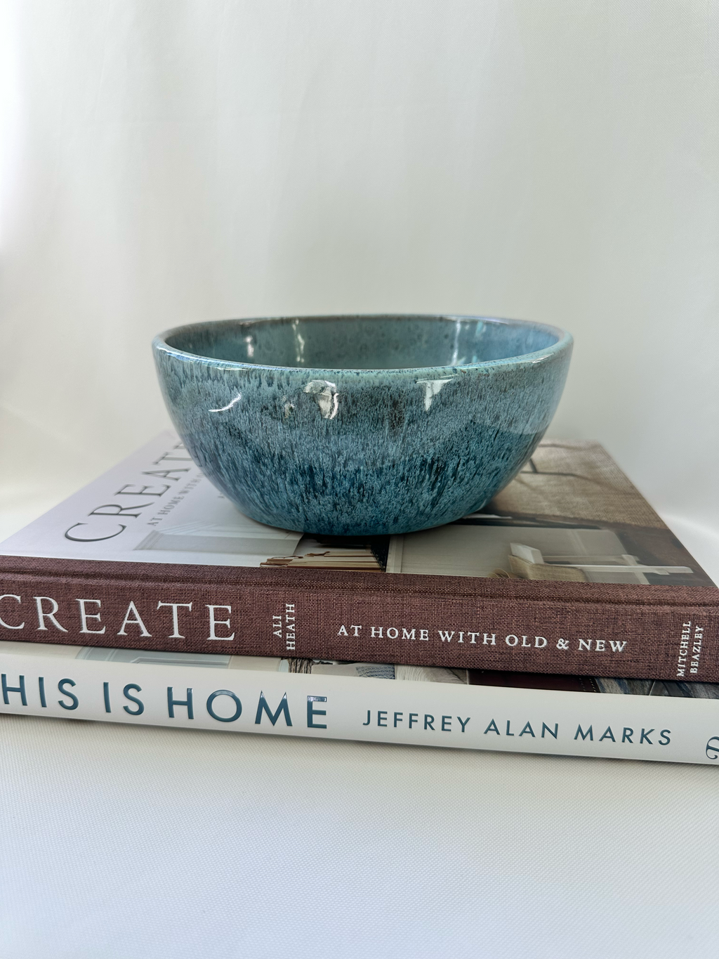 Mottled blue studio pottery planter displayed on stacked design books, showing its shallow rounded form and glossy variegated glaze.