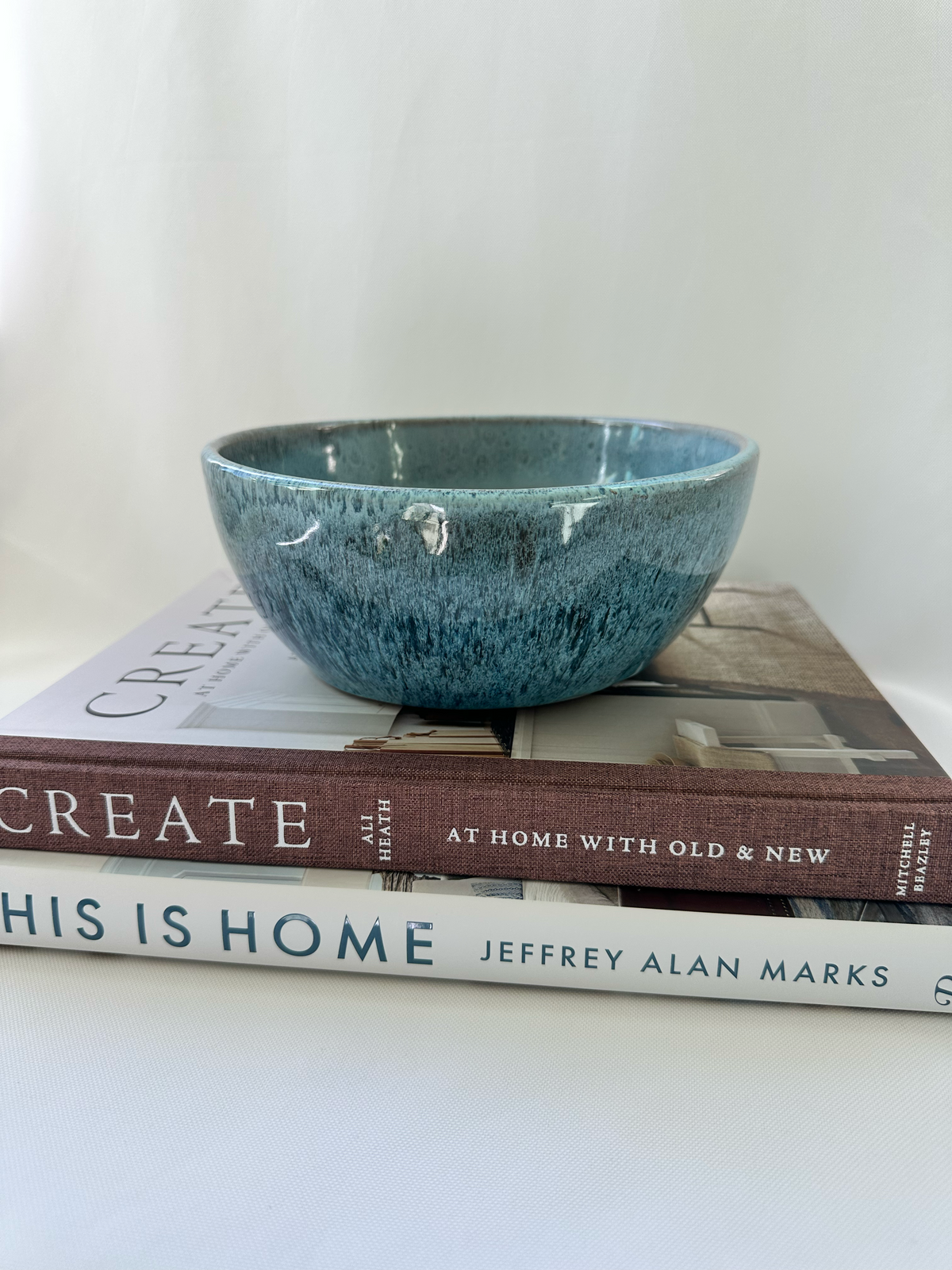 Mottled blue studio pottery planter displayed on stacked design books, showing its shallow rounded form and glossy variegated glaze.