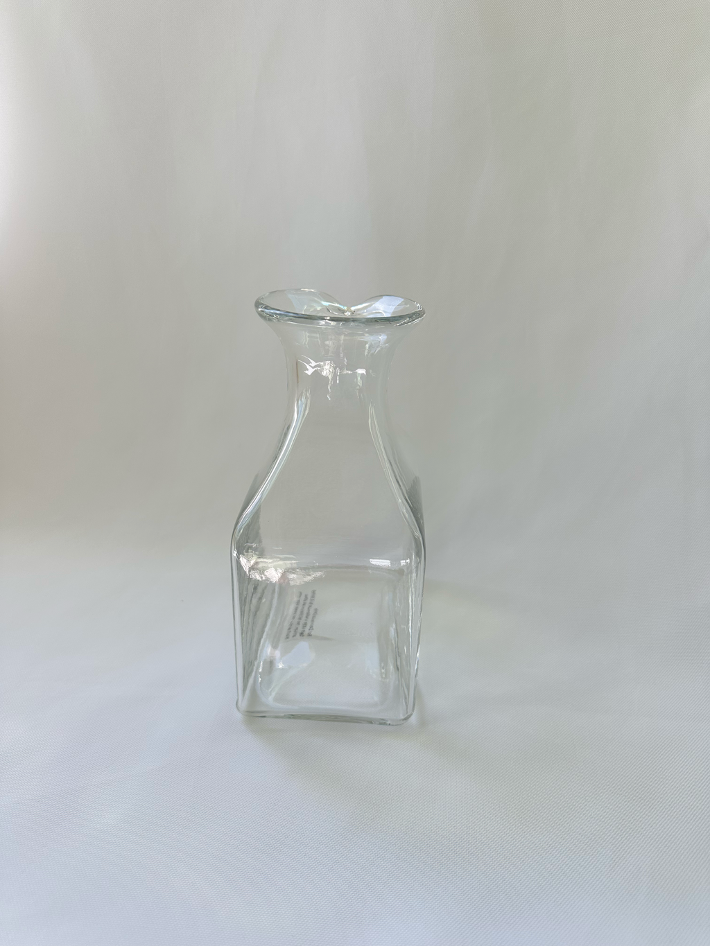 Front view of handmade clear glass vase with square lower body, sloping shoulders, and asymmetric rolled rim.