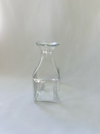 Front view of handmade clear glass vase with square lower body, sloping shoulders, and asymmetric rolled rim.