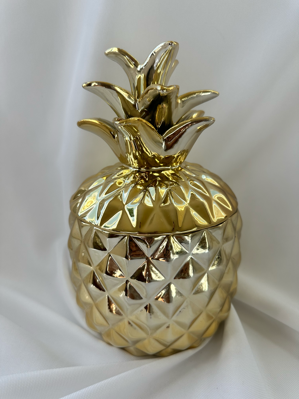 Hazel & Co gold-tone ceramic pineapple decorative container with faceted body and sculptural leafy lid.

