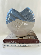 Blue and off-white sculptural ceramic vase displayed on stacked interior design books for scale.
