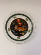 A round clear glass plate featuring a hand-painted central design of a leopard on a black background, surrounded by orange flowers and green leaves, with a dark green ring border.