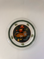 A round clear glass plate featuring a colorful printed design of a leopard, flowers, and green leaves on a black background, with a dark green inner border.