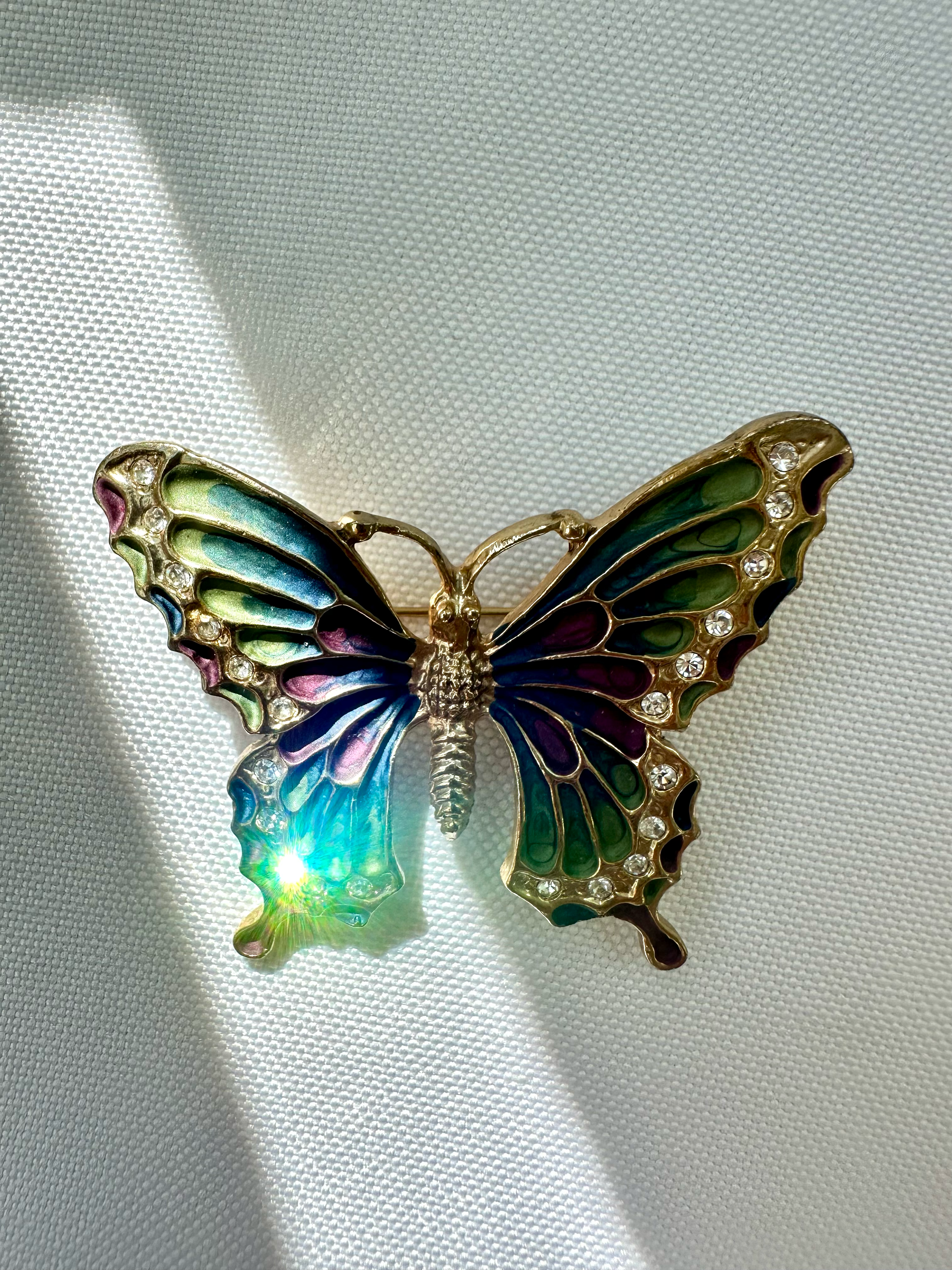 Butterfly brooch in sunlight with teal, green and plum enamel and reflective clear crystals.
