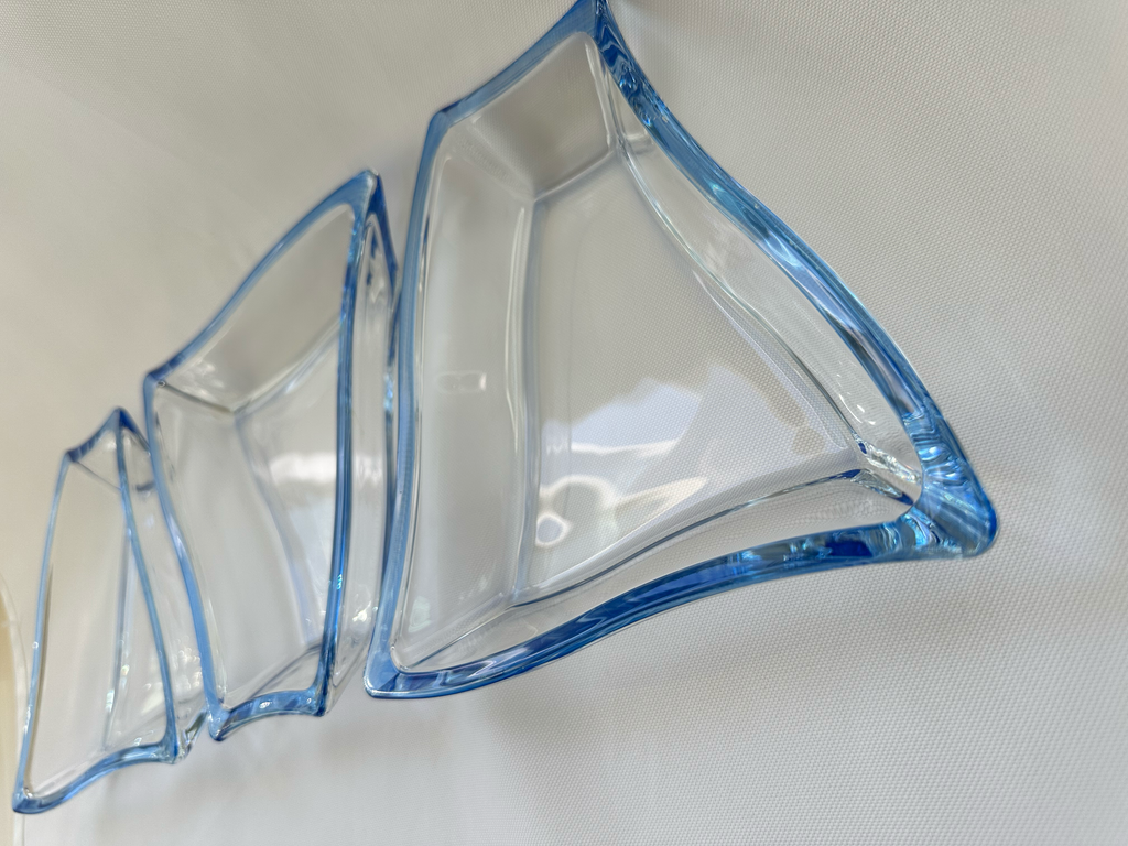 Angled close-up of three clear asymmetrical serving dishes highlighting their curved forms and blue glass edges.