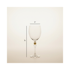 A clear wine glass with a small gold accent at the base of the stem, shown on a light beige background with dimension lines indicating 3 inches wide at the bowl and 8 inches tall.