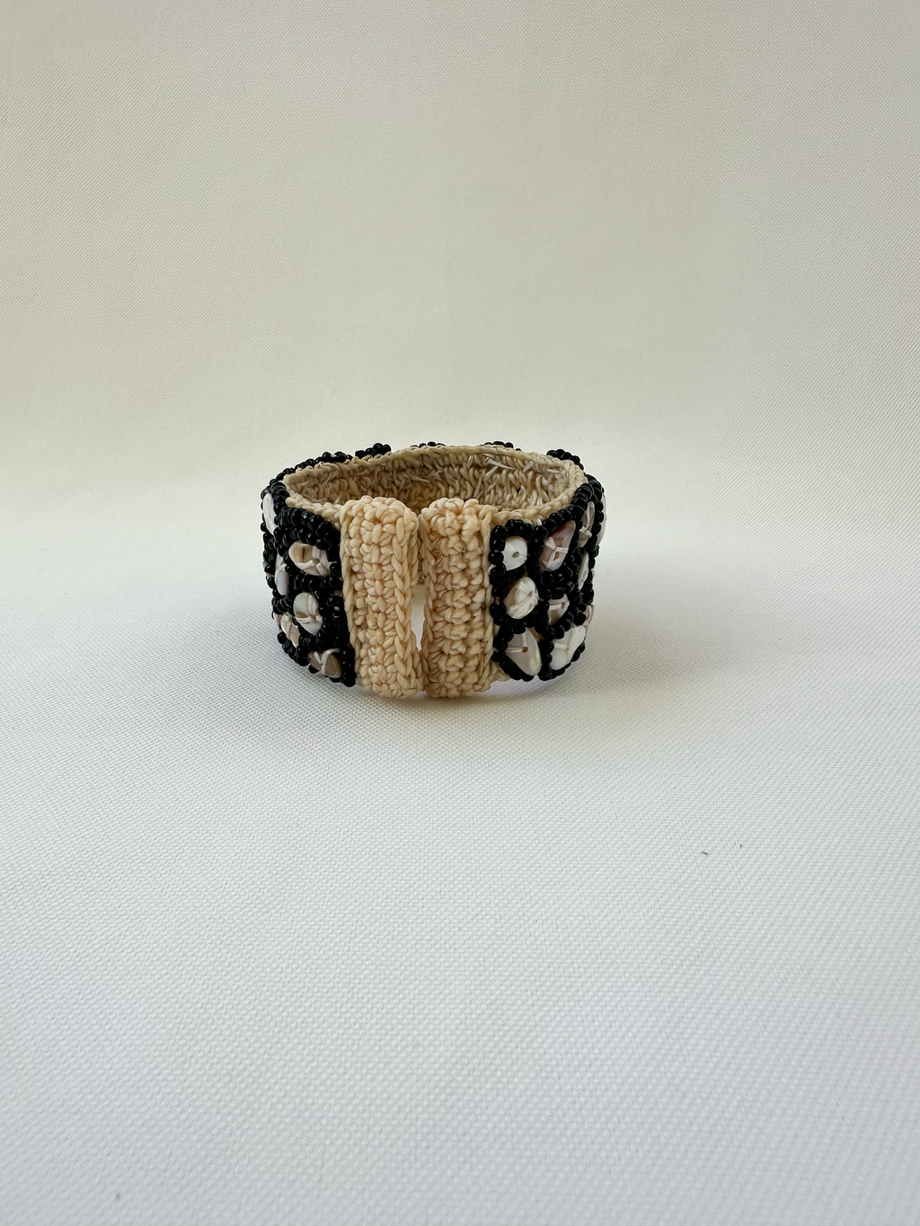 Rear view of cream woven open cuff bracelet showing the flexible open ends and black beaded shell decoration.
