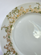 Close-up of Haviland Chambord plate showing green botanical motifs and ornate gold scrollwork around the rim.
