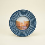An ivory studio background featuring a round blue and white patterned picture frame with an insert reading Cynthia Rowley New York 4 in x 4 in.  