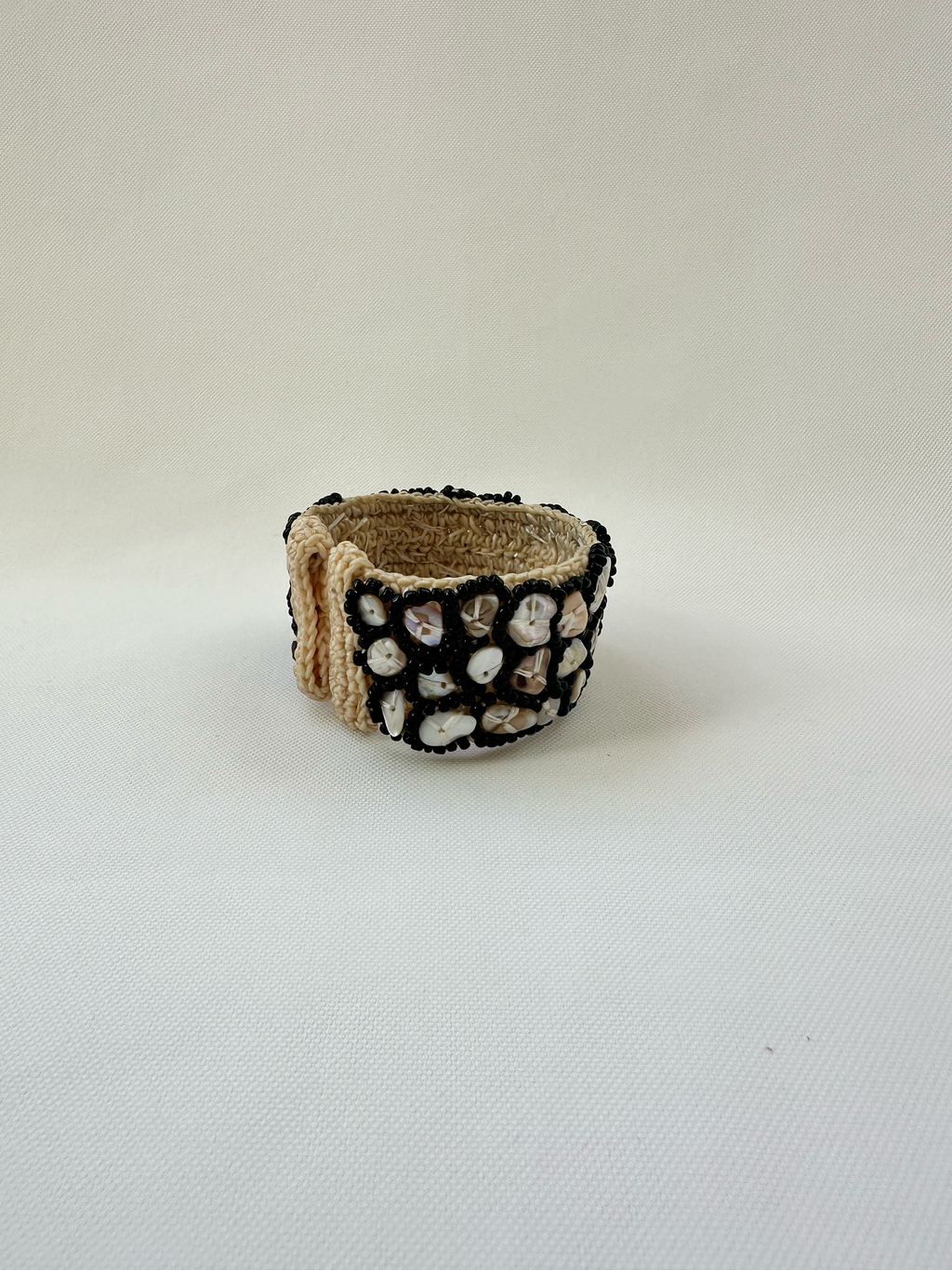 Side view of shell and black beaded cuff bracelet showing woven cream construction and dimensional beadwork.
