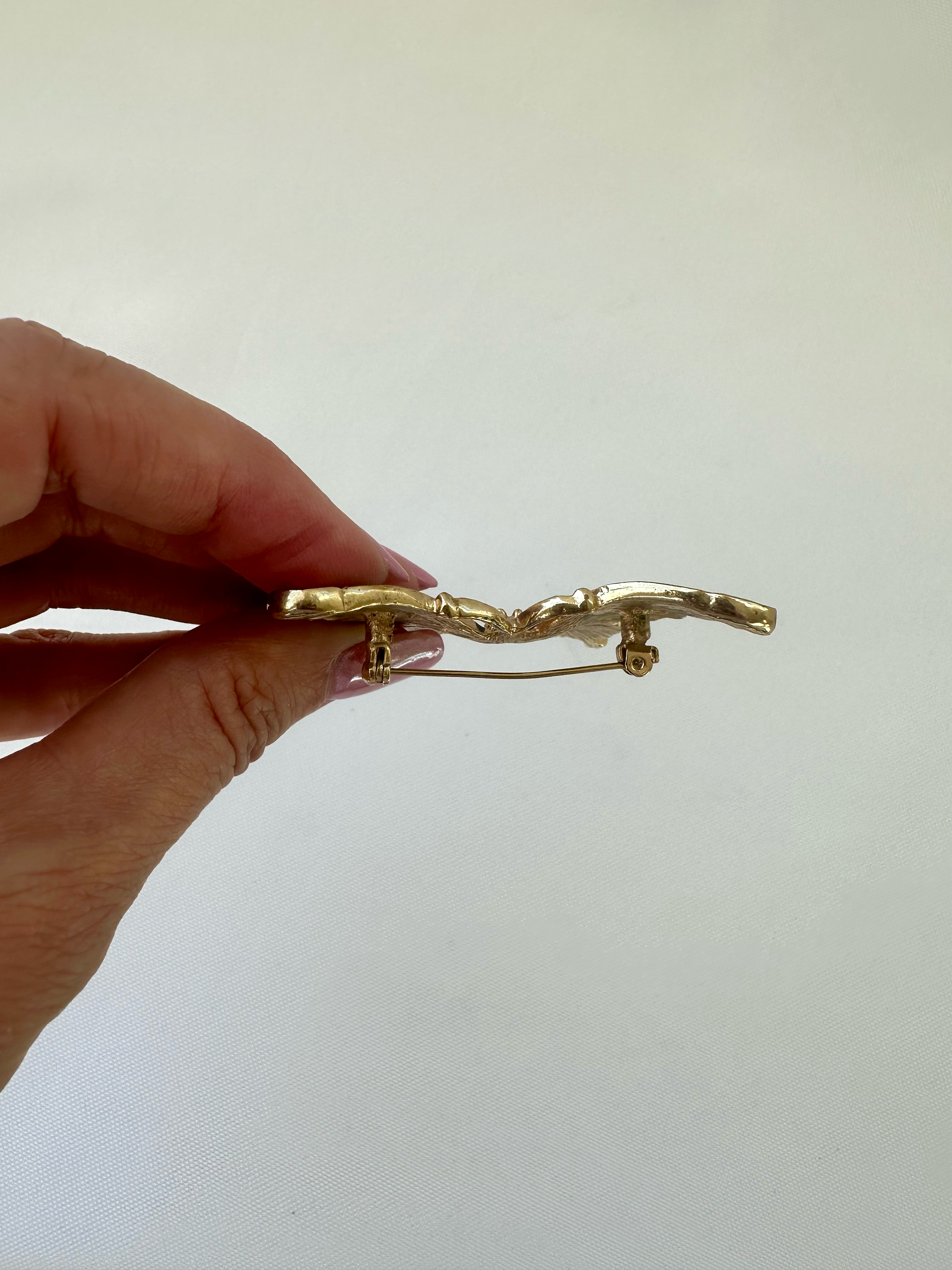 Side view of butterfly brooch held in hand showing its profile and pin clasp construction.
