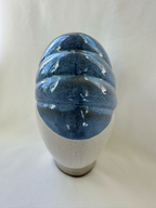 Side view of sculptural ceramic vase showing raised blue diagonal bands over the off-white body.
