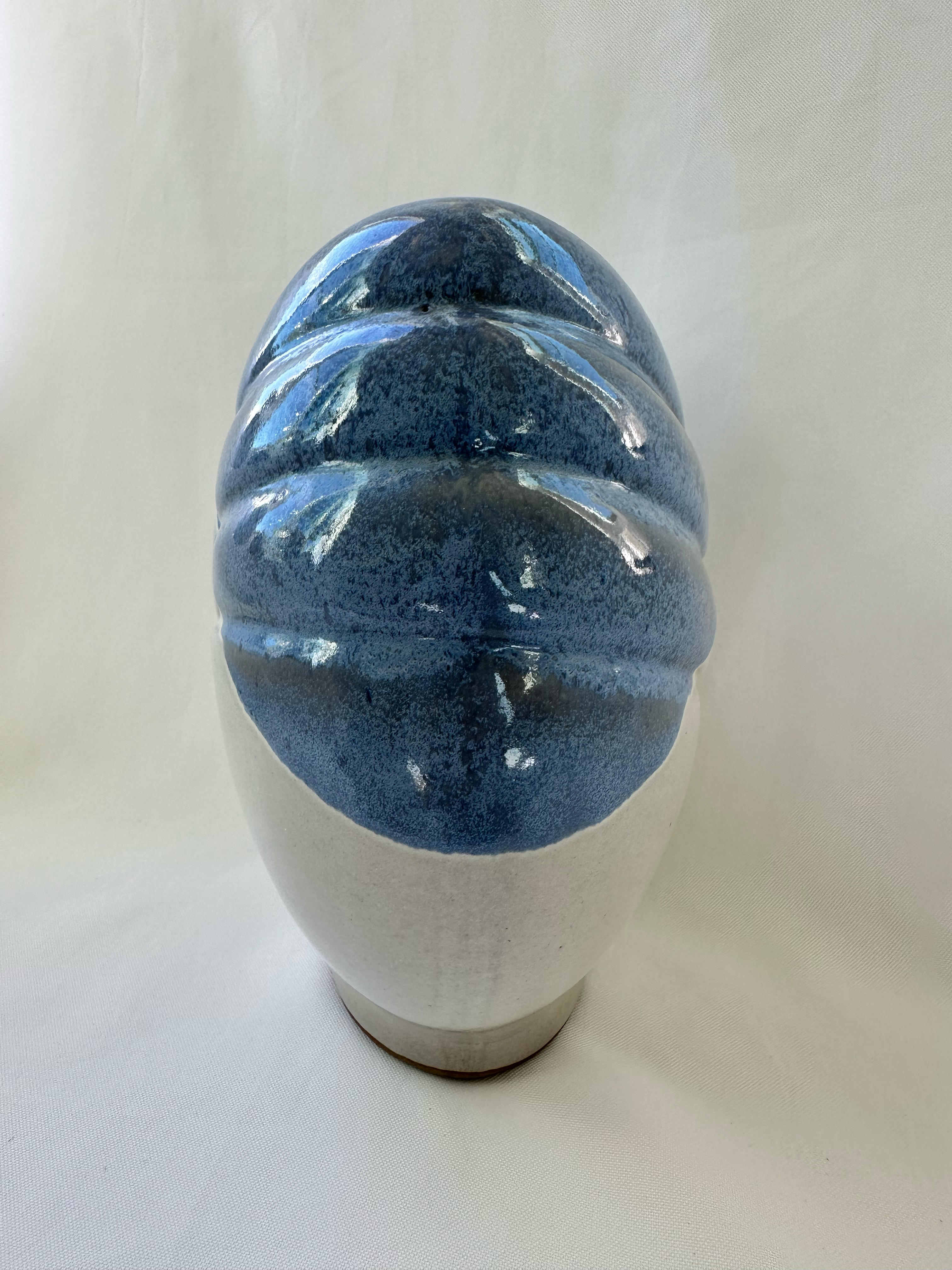 Side view of sculptural ceramic vase showing raised blue diagonal bands over the off-white body.
