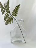 Handmade clear glass vase with sculptural pour-spout rim styled with a single fern stem.