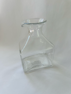 Three-quarter view of clear glass decorative vase showing its sculptural profile and pour-spout-style rim.
