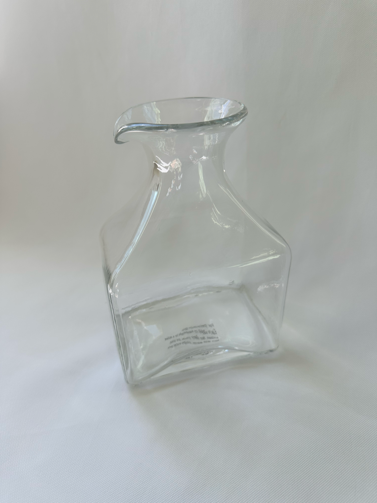 Three-quarter view of clear glass decorative vase showing its sculptural profile and pour-spout-style rim.
