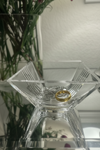 Tiffany & Co. Metropolis crystal bowl with jewelry inside of it, sitting on a mirrored table with soft lamp light, flower stems in the background. 
