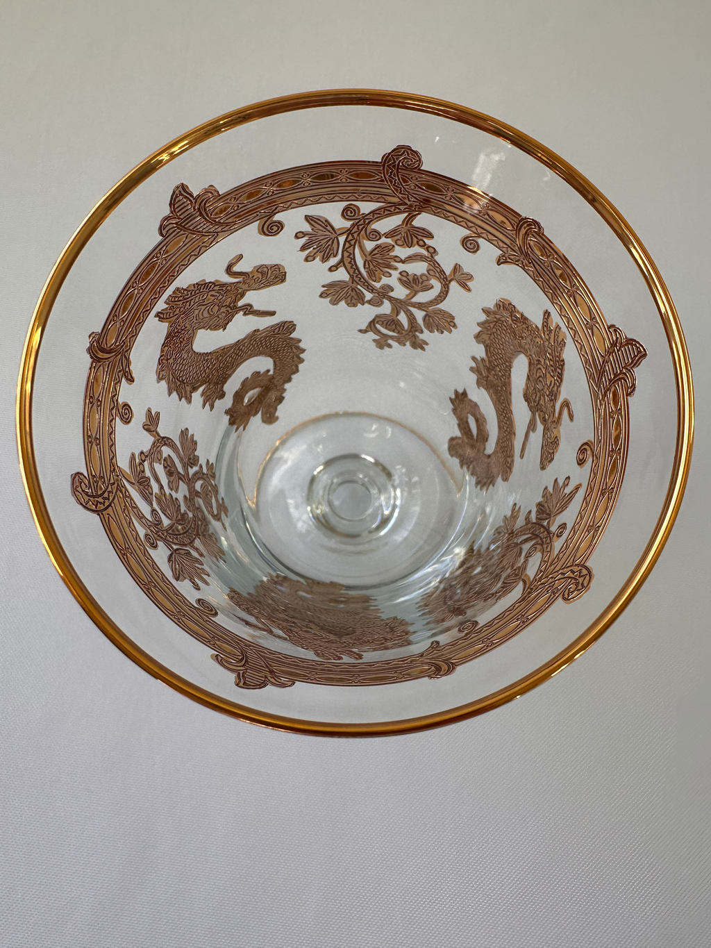 A clear glass and gold goblet viewed from above, featuring a gold rim and an intricate brown printed design of dragons and scroll motifs.