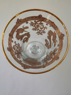 A clear glass and gold goblet viewed from above, featuring a gold rim and an intricate brown printed design of dragons and scroll motifs.