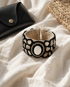 Woven shell and black beaded cuff bracelet styled with white linen, black clutch and woven straw bag.