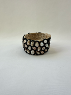 Angled view of woven cuff bracelet showing irregular nacreous shell pieces framed with glossy black seed beads.