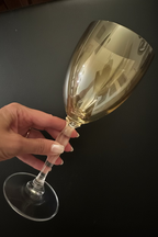 A hand holding a clear wine glass with a reflective gold-toned tint against a dark background.