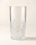 A clear cut-crystal tumbler with ornate floral and scrollwork engravings around the lower half, photographed on a warm off-white background.
