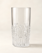 A clear cut-crystal tumbler with ornate floral and scrollwork engravings around the lower half, photographed on a warm off-white background.